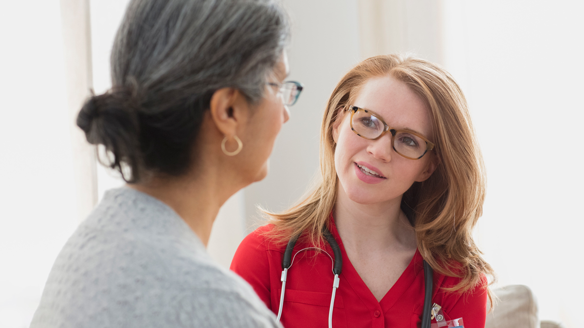 A young doctor tilts her head and with direct eye contact listens intently to an older woman speaking to her