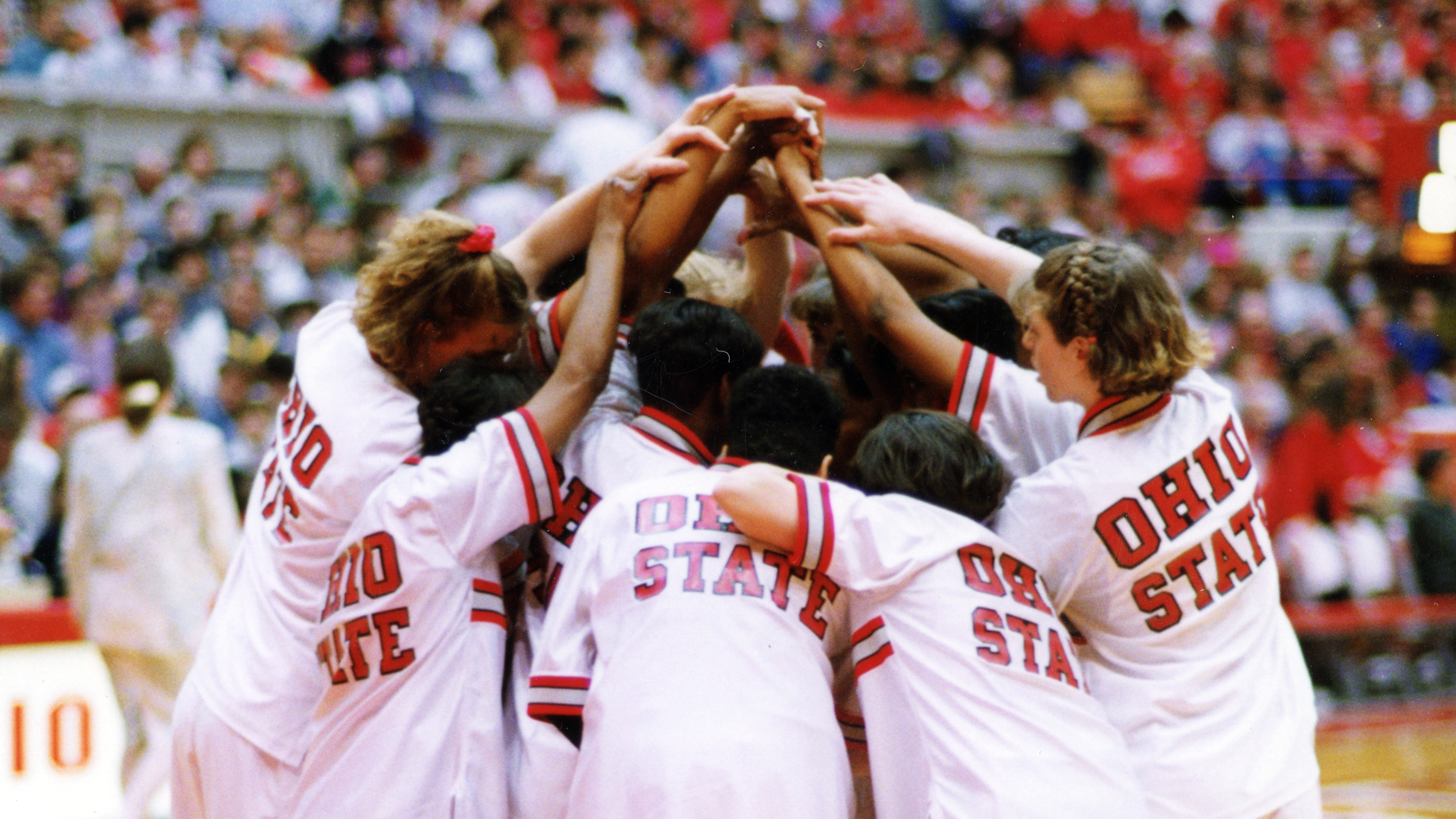 In their white warmups with Ohio State proudly displayed across their backs, at least 10 Black and white players huddle together with their arms upstretched. The photographer was behind them so no faces appear in the photo.