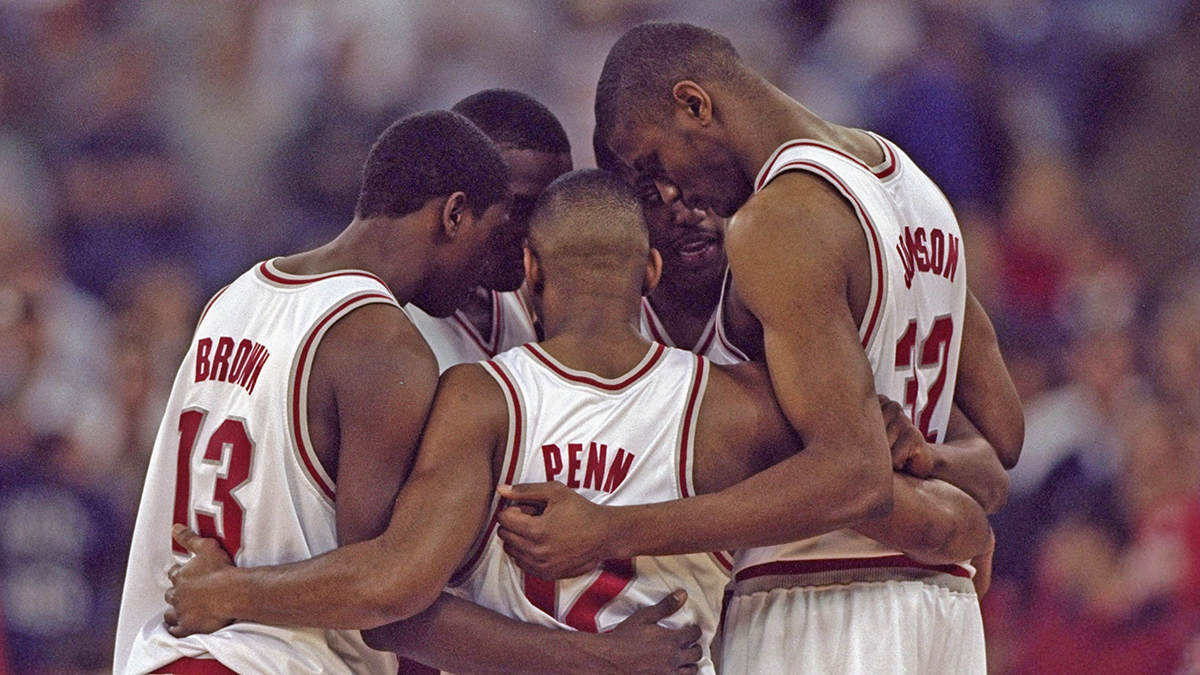 Five Ohio State players huddle with their arms around one another in a moment when play pasued on the basketball court. All are black men and varying degrees of tall.