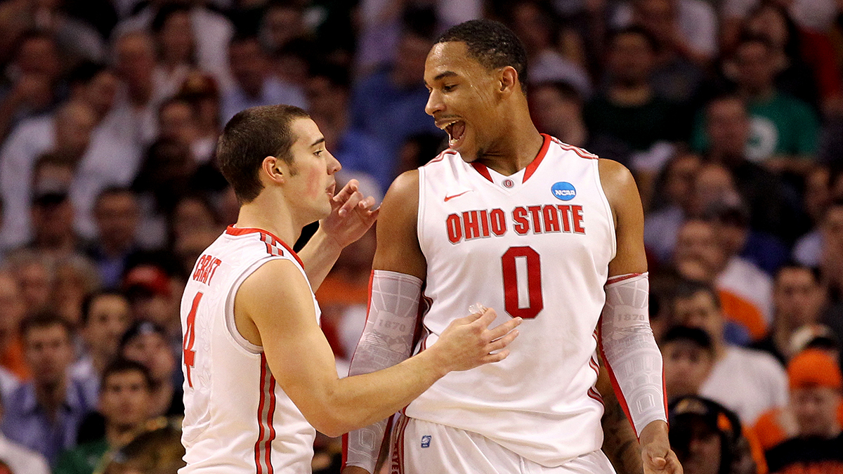 Two Ohio State men’s basketball players talk on the court. The shorter white man looks serious as he keeps an eye on something out of the photo frame. The taller black man looks at him and speaks confidently. 