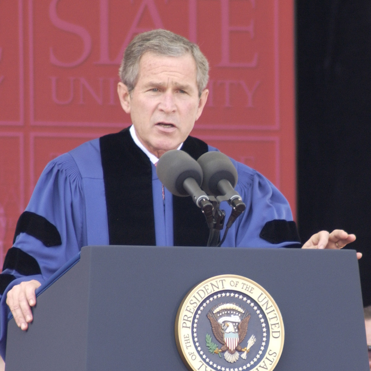 Former President George W. Bush speaks at a lectern wearing grad  robes.