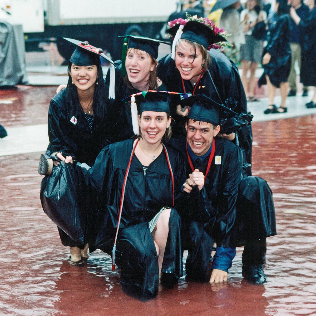 Five people in caps and gowns pose together in several inches of standing water.