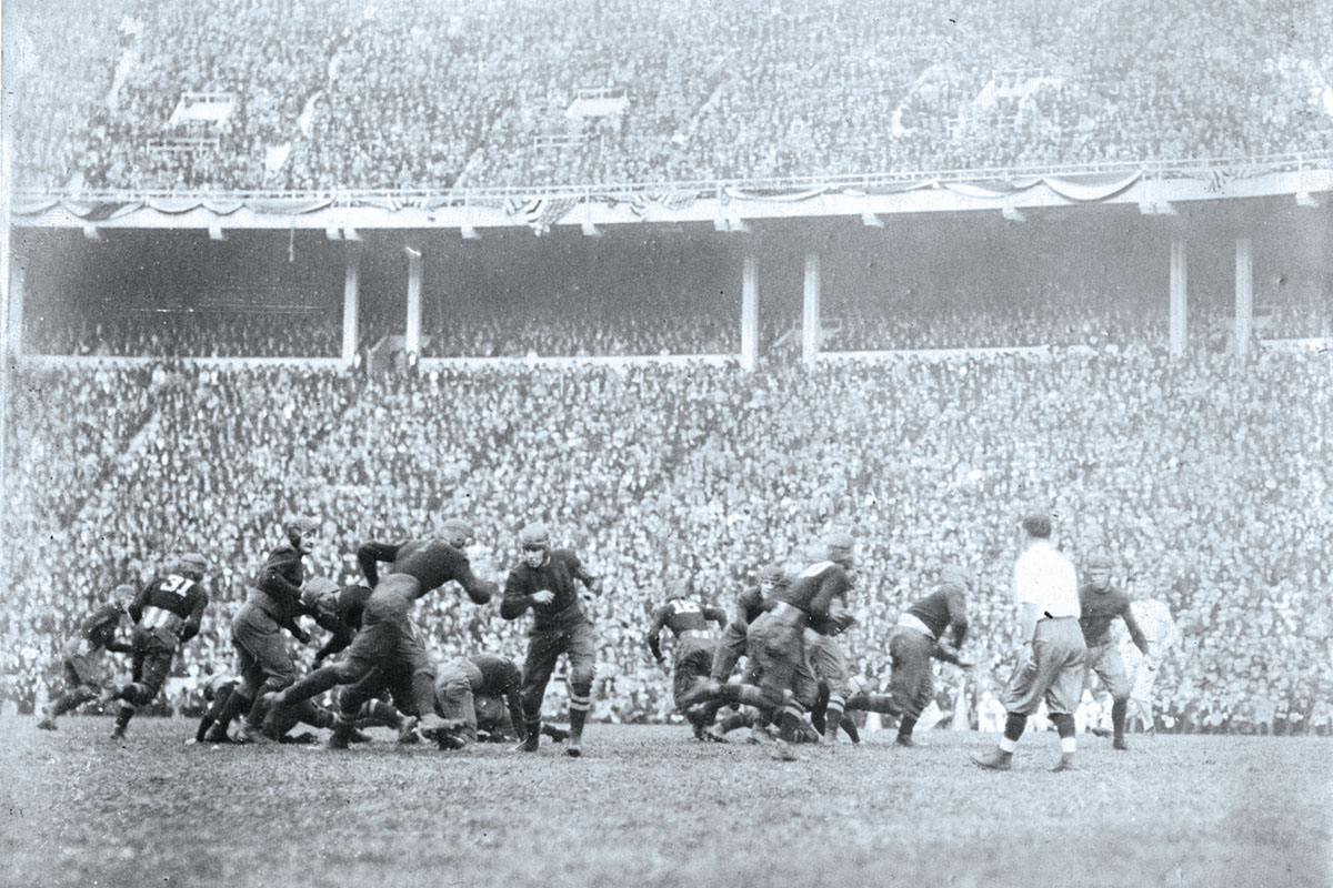 An old-time football game has players in soft helmets and little padding. Behind them, Ohio Stadium’s stands are packed.
