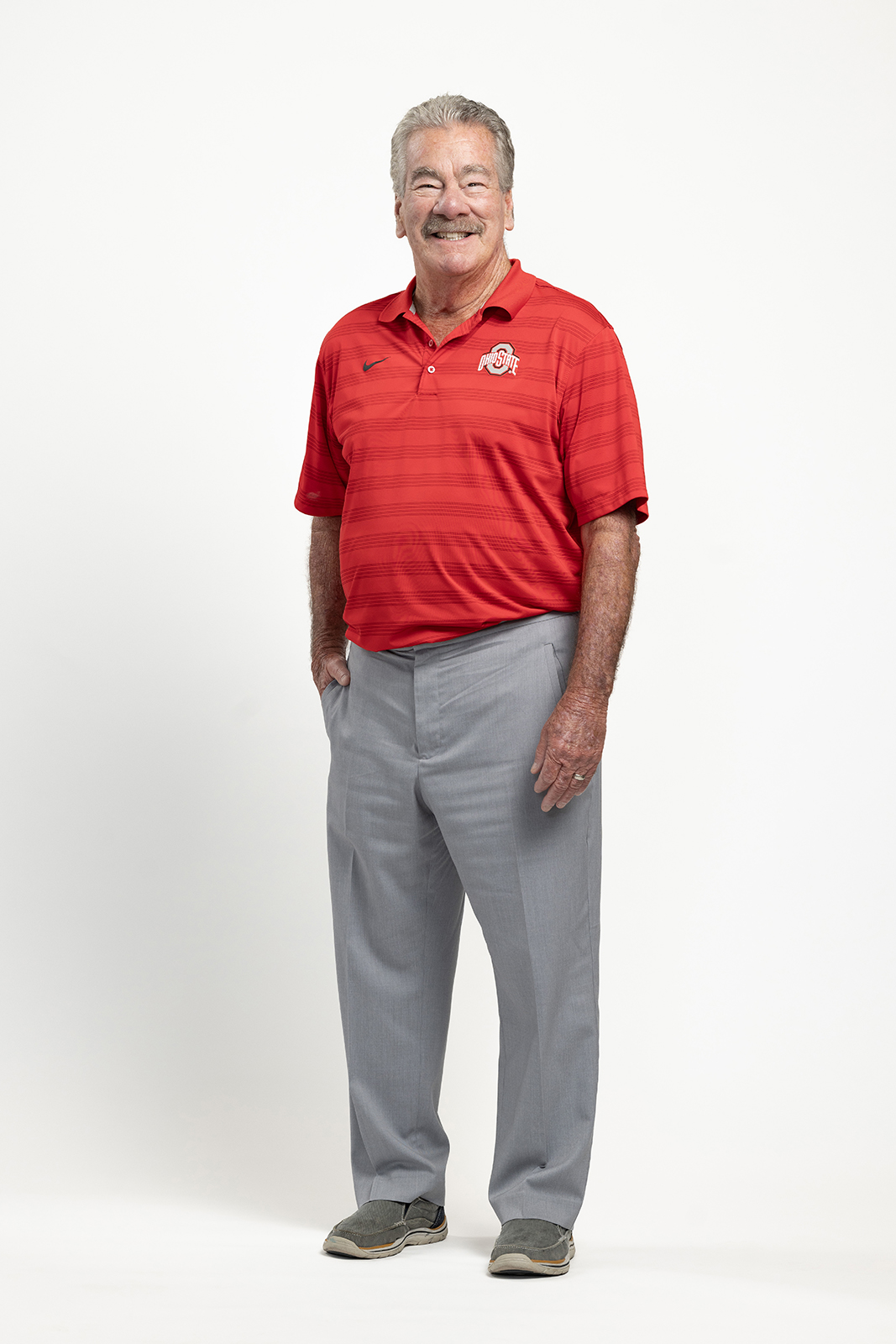 James “JT” Terranova grins for a portrait and stands with one hand tucked in a pocket and the other by his side. He wears an Ohio State golf shirt and dress pants, and is a white man with graying hair and a facial expression and smile so friendly, he could pass as a good Santa Claus actor, if you added long white hair and beard. Instead, he’s neatly trimmed.