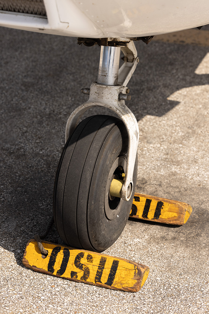 One wheel of a small aircraft is shown with the yellow chocks above placed around it. These triangles keep the plane from unintentionally rolling.