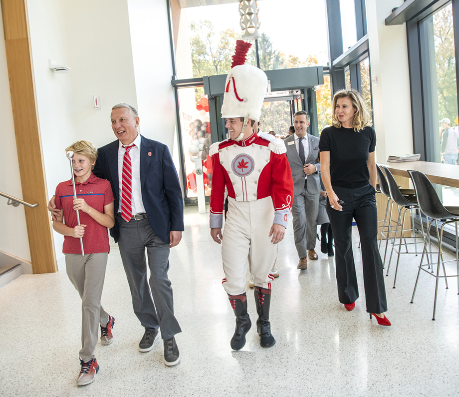 Four people lead more inside a building with shiny floors and a wall of windows. The four are all smiling: The dad has an arm slung around his son's shoulders, and the boy is carrying the drum major's baton. The fourth person is the boy's mom. She's wearing scarlet heels and a proud expression as she watches.