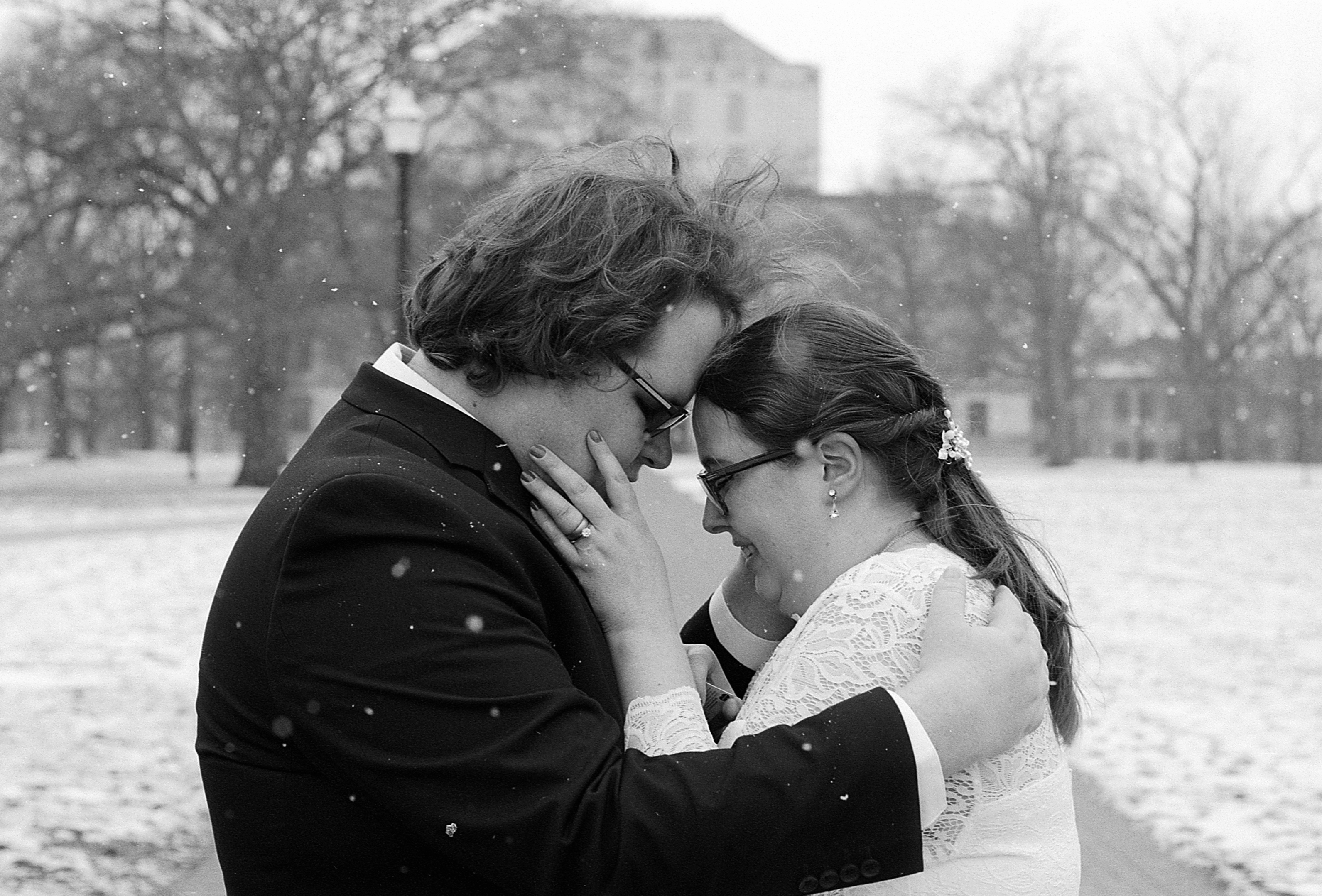 A bride and groom touch foreheads on The Oval as it snows in this black and white photo.