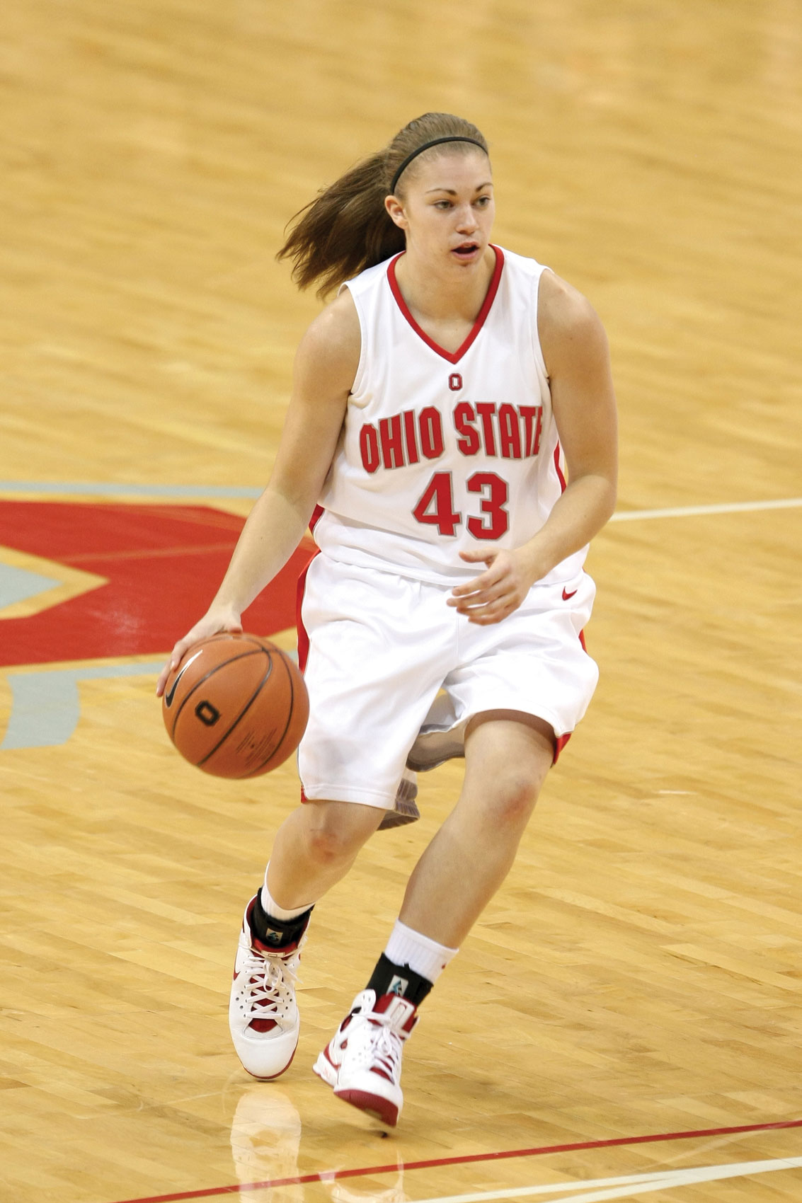 As an Ohio State basketball player, Sarah Schulze dribbles the ball during a game. She wears a headband and ponytail and her jersey number was 43.