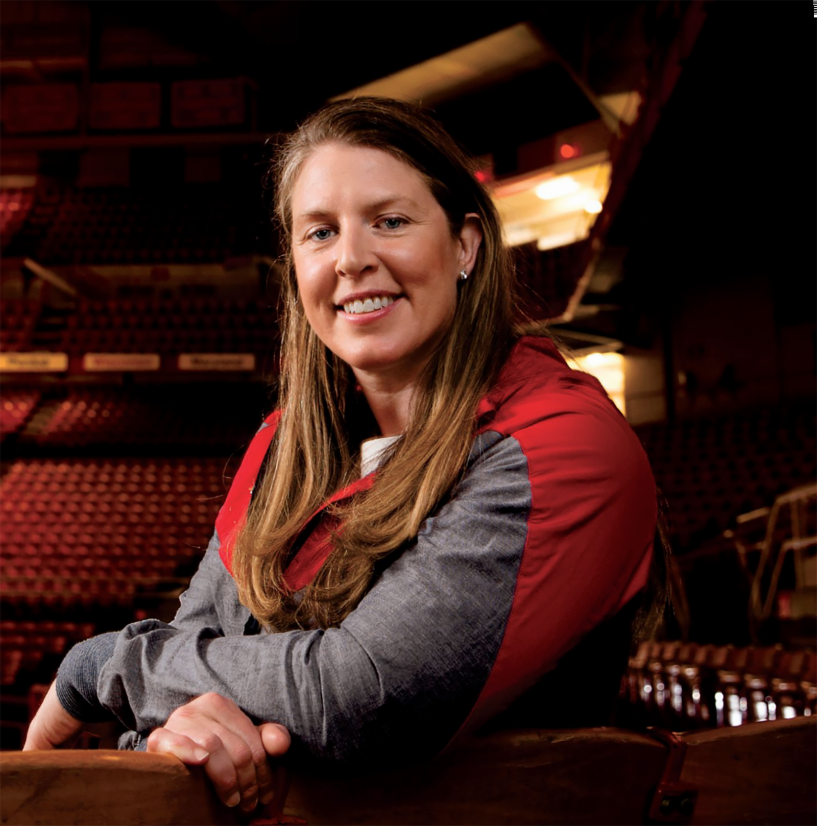 Katie Smith, a blue-eyed, long-haired white woman, sits in the stands of St. John Arena. The way she's smiling suggests she's friendly and a good listener.