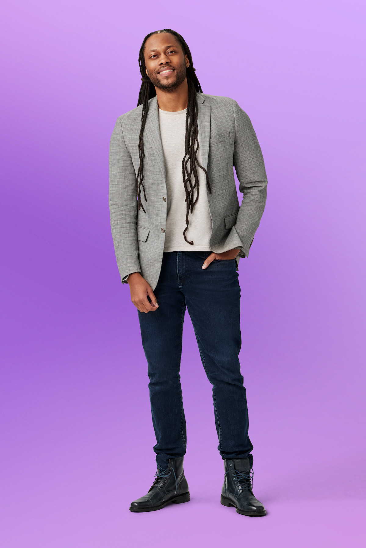 Victor St. John, a black man with long dreadlock hair, wearing a blazer and jeans, looks friendly and studious—like he'd be the coolest professor—as he poses for this photo.  