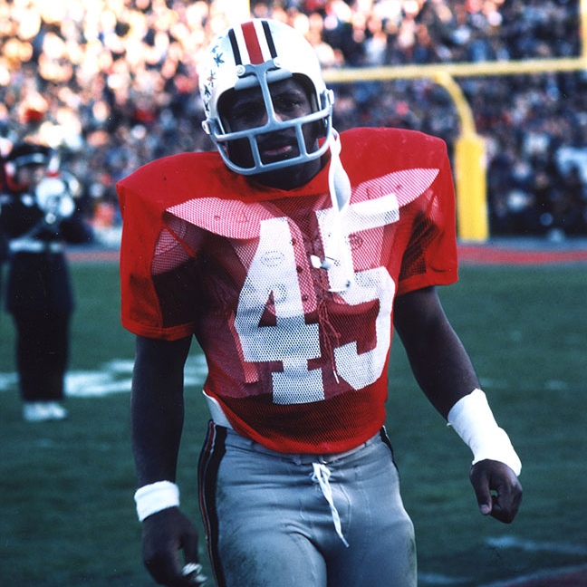 On the football field with packed bleachers behind him is Griffin, photographed during a moment between plays in a game. He looks tired and his left wrist is taped up.