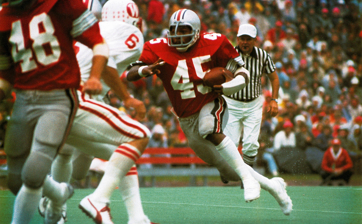 A player wearing the number 45 sprints while tucking a football against his side as a player from the opposing team attempts to get in his way.