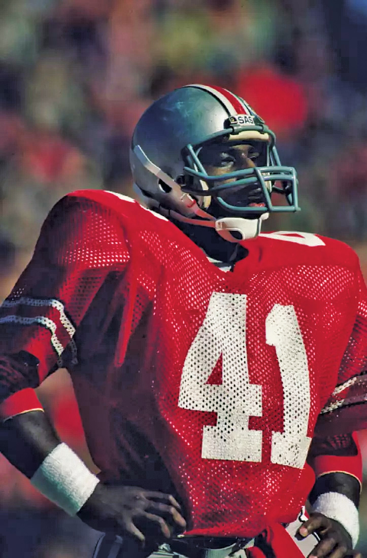 Keith Byars stands with hands on hips in his football uniform in the midst of a game