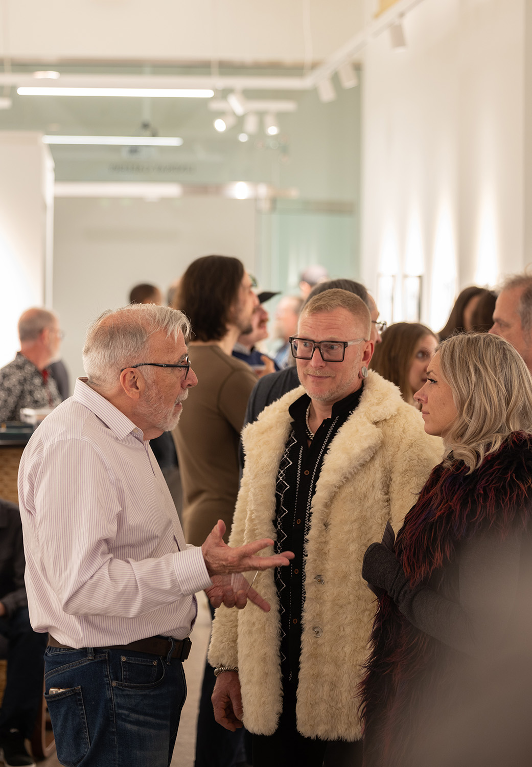 Duff Lindsay speaks with two gallery-goers. They're both wearing hip-length furry or fuzzy coats.