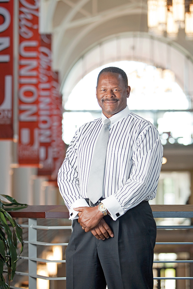 Dressed in a striped dress shirt, tie and dress pants, Moody smiles as he poses on the second floor of the student union