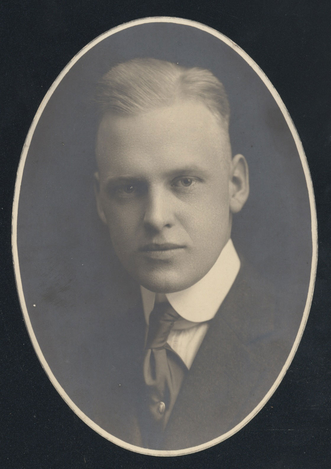 An old photograph shows a light-haired young white man in a suit. He's staring piercingly into the camera with a serious expression, as was common in old photos.