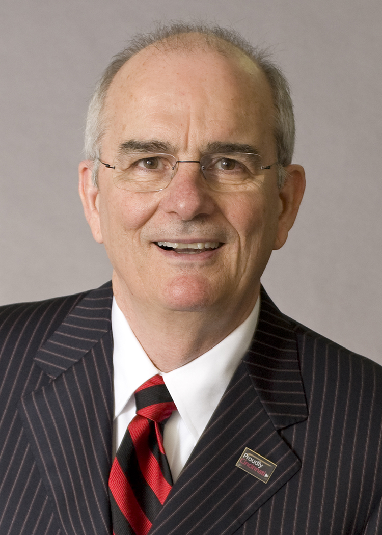 Gregory Williams wears glasses, a suit and an open mouthed smile. He looks like he's laughing as he poses for this formal portrait.