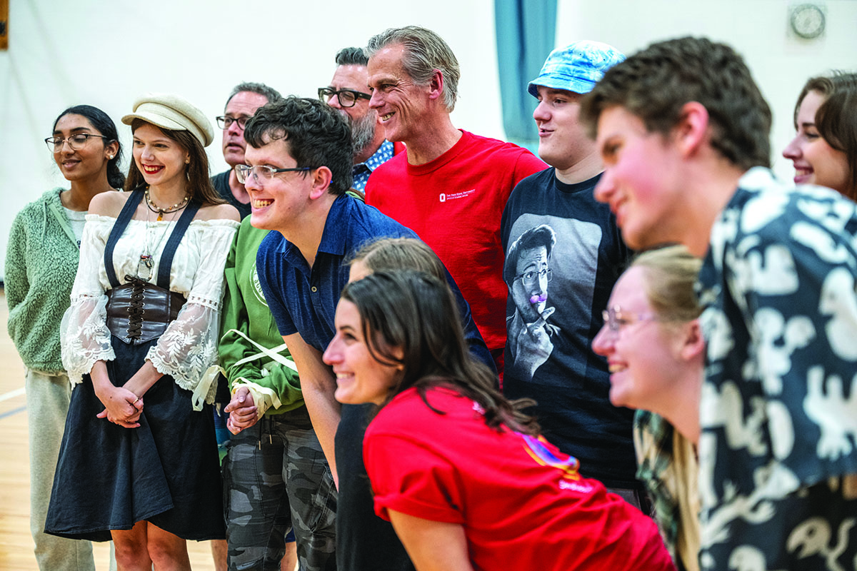 associate professor Kevin McClatchy grins as he poses with teens and college students who took and helped with a Shakespeare in Autism session. Everyone has big smiles.