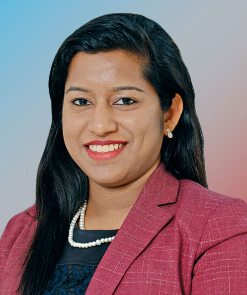 A woman of Indian descent with long hair, pretty earrings and a suit coat smiles for a headshot.