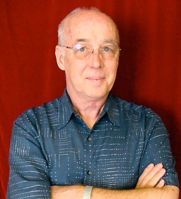 As an older man, Strickler smiles more with his eyes than his mouth in this headshot. He's a balding white man wearing rimless glasses and a blue patterned button down shirt.
