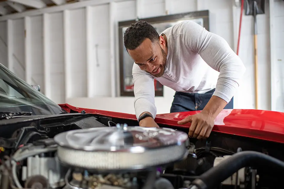 man in white shirt works on car engine in a garage