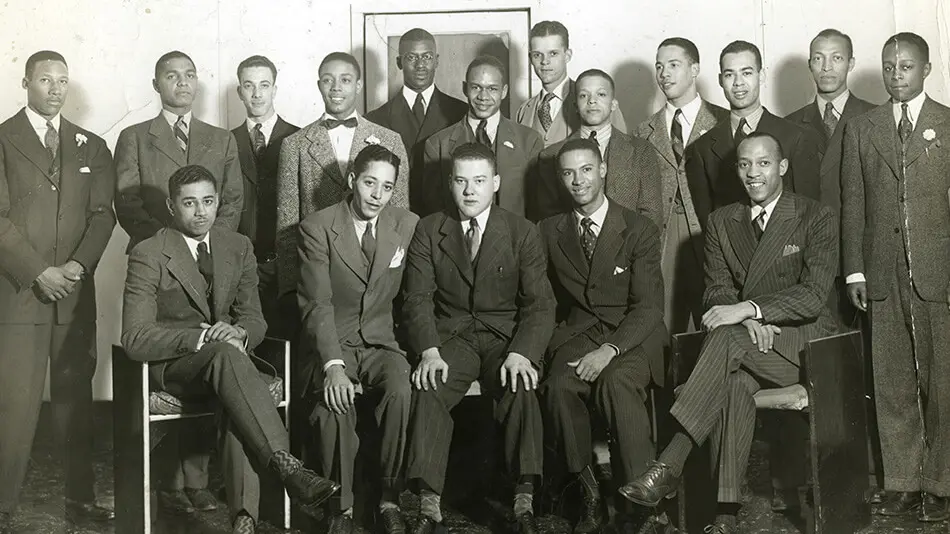 Black and white photo of member of Alpha Phi Alpha, in suits. Men are in two rows, front row seated, back row standing.