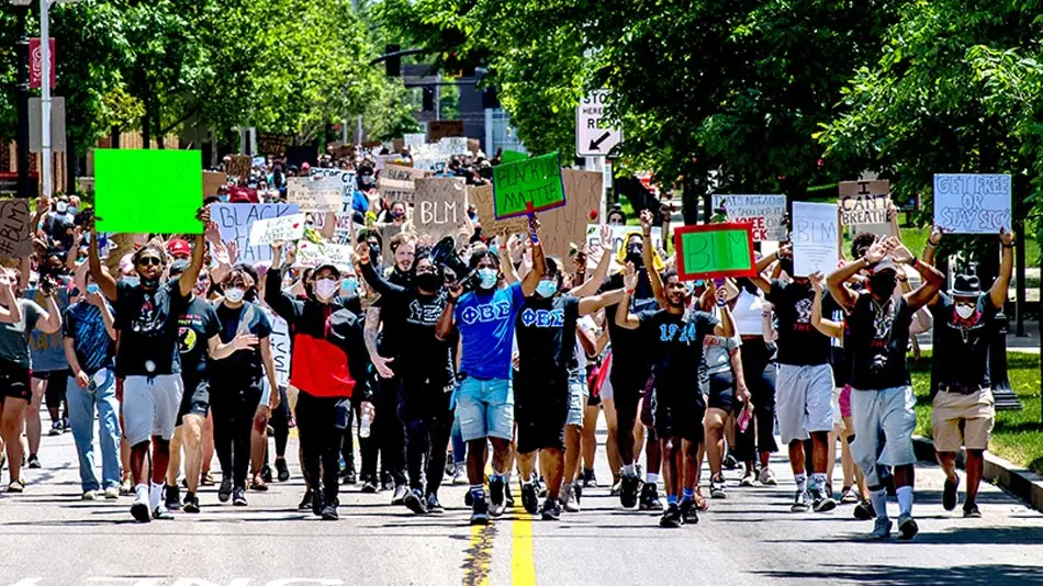Color photo of a diverse group of students waking on road holding BLM signs, protesting the killing of George Floyd and other victims of police brutality. 