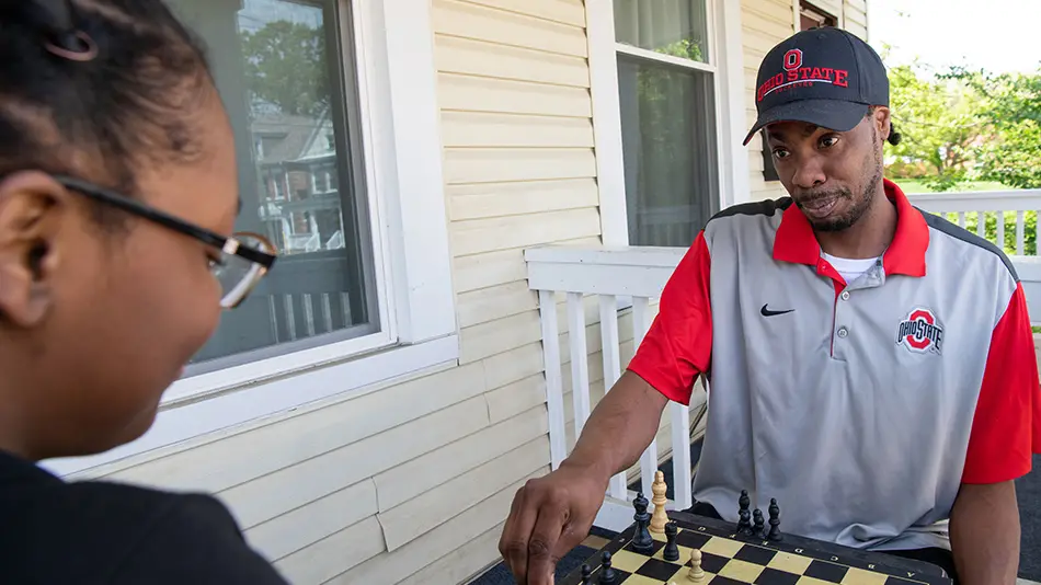 A dad and his high school daughter are sitting on a porch playing chess. 