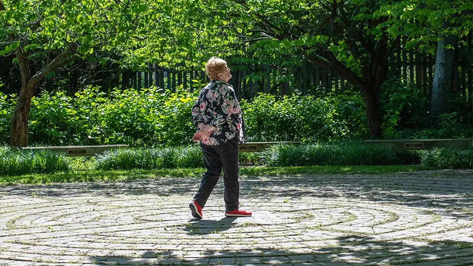 A woman walks along a brick labyrinth through the trees of Chadwich Arboretum.