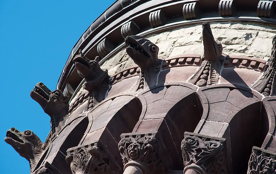 Architectural details from a stone bell tower featuring animal heads on the exterior surface