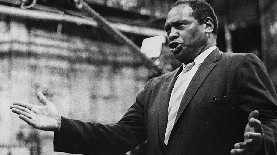 Black and white historic photo of Paul Robeson. He is singing with his arms slightly raised to the sides.