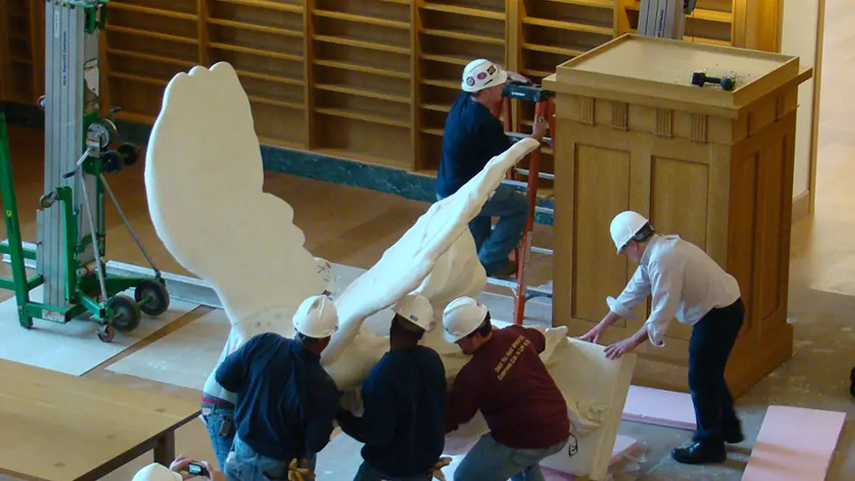 The Nike of Samothrace statue is being returned to Thompson Library by men in hardhats.