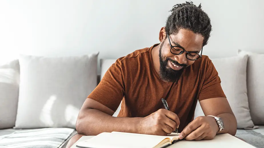 Man wearing glasses and smiling writing in a notebook 