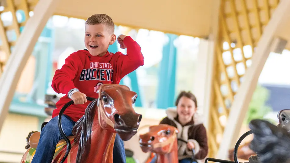 Young boy wearing a red OSU sweatshirt riding a fake horse as part of the Cedar Downs Racing Derby at Cedar Point.