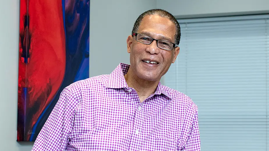 Headshot of man wearing glasses in a pink checked shirt in front of an red and blue abstract art
