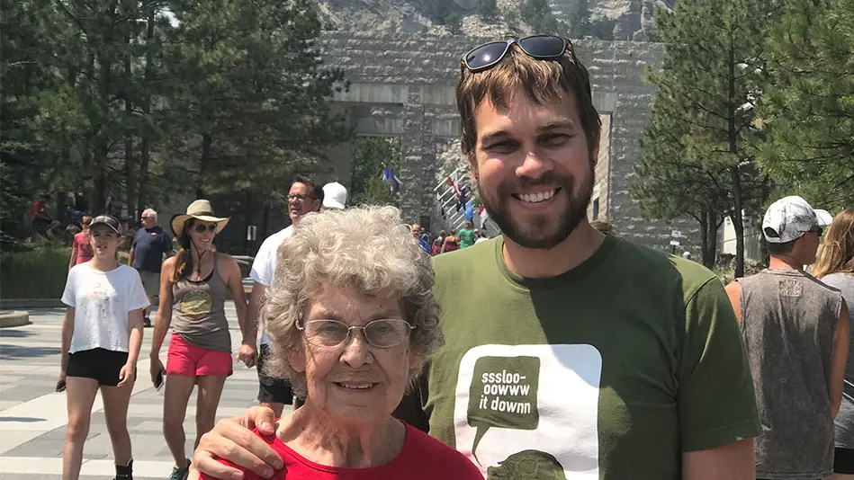 Brad is standing with his arm around Grandma Joy as they visit the Mount Rushmore National Memorial