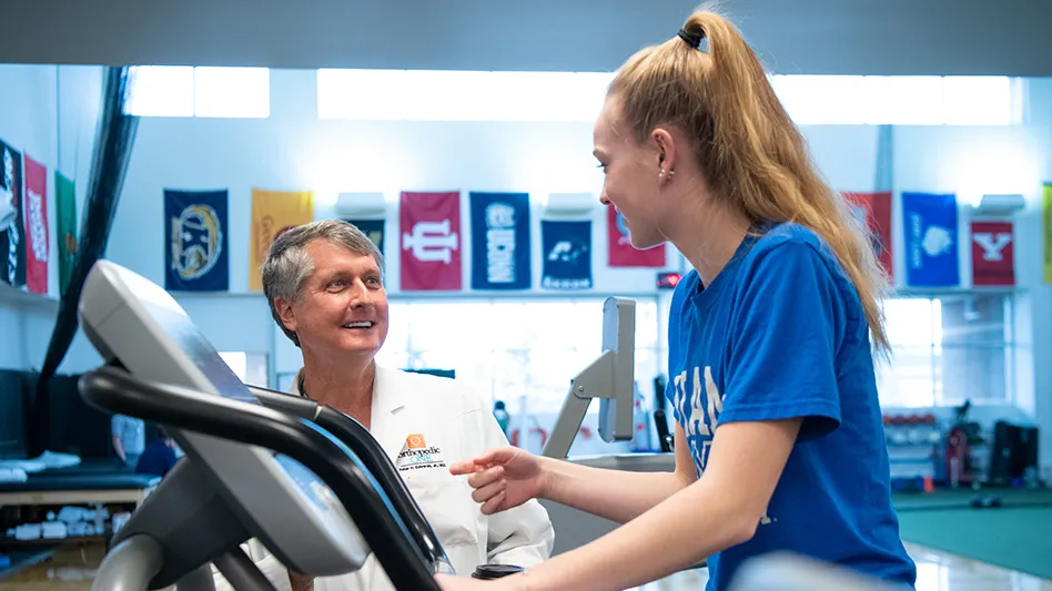 Edwards is standing next to a young woman on a treadmill.