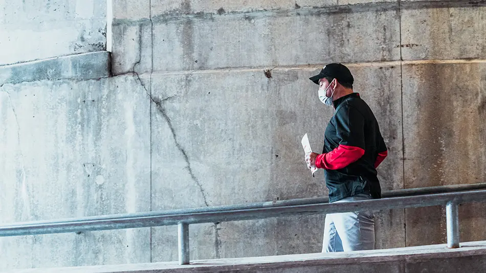 Ryan Day is wearing a face mask and walking down a ramp next to a cement wall.