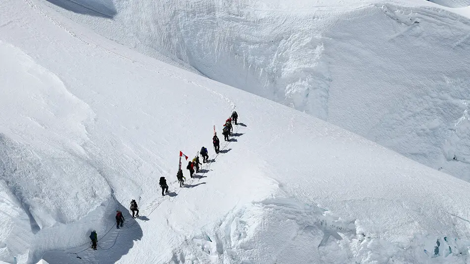 a line of people hike up a mountain covered in deep snow