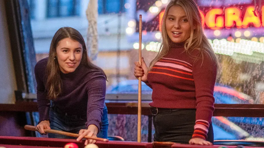 Two young women are playing pool. 