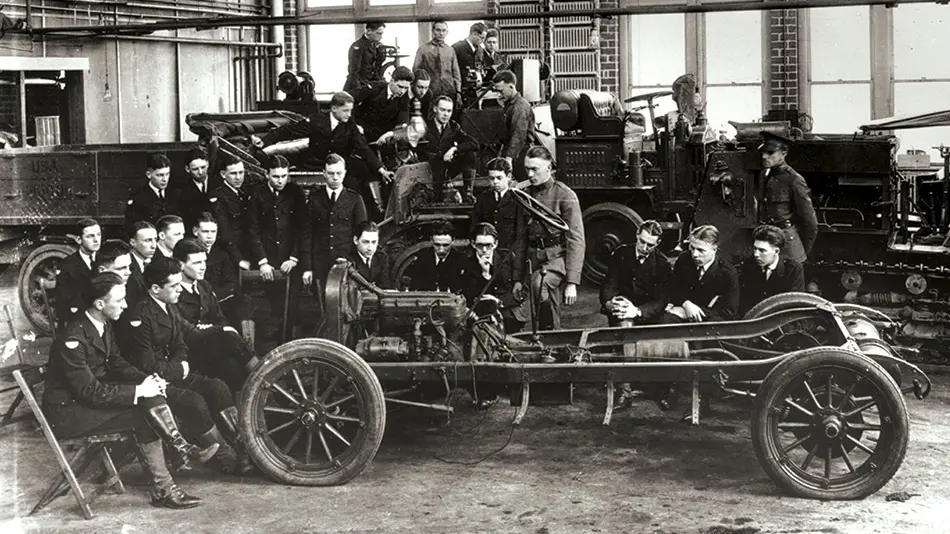 Black and white archival photo of a large group of student mechanics from 1918 gathered around a vehicle.
