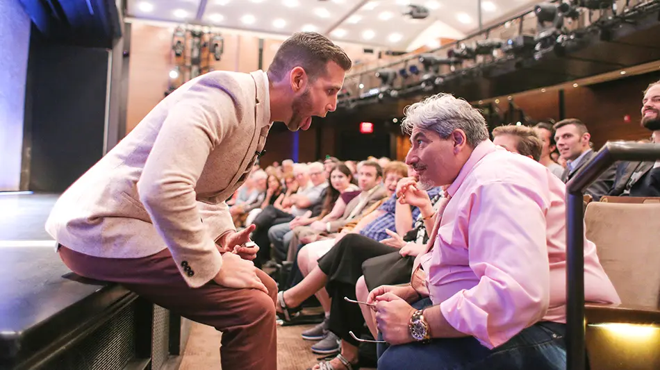 Joshua Jay performing a magic trick for a man in a pink shirt seated in the audience