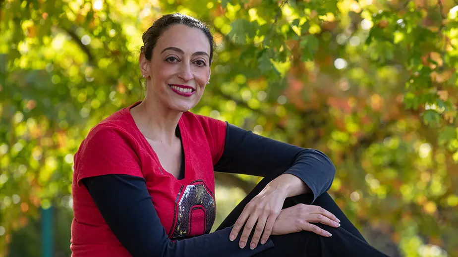 Portrait of Rosa Ailabouni sitting outside wearing a red Ohio State shirt, a black long sleeve shirt, and black pants.