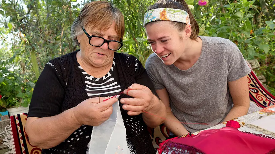 woman stitches embroidery as a younger female watches