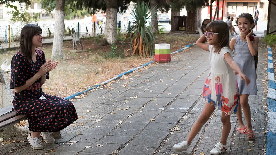 woman sits on bench as two girls play