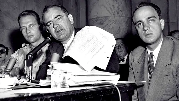 black and white image of Senator McCarthy and two other individuals in front of a microphone