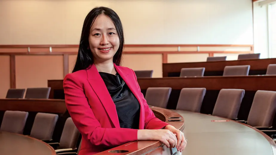 A woman in a red suit smiles in a classroom built to focus attention on the speaker