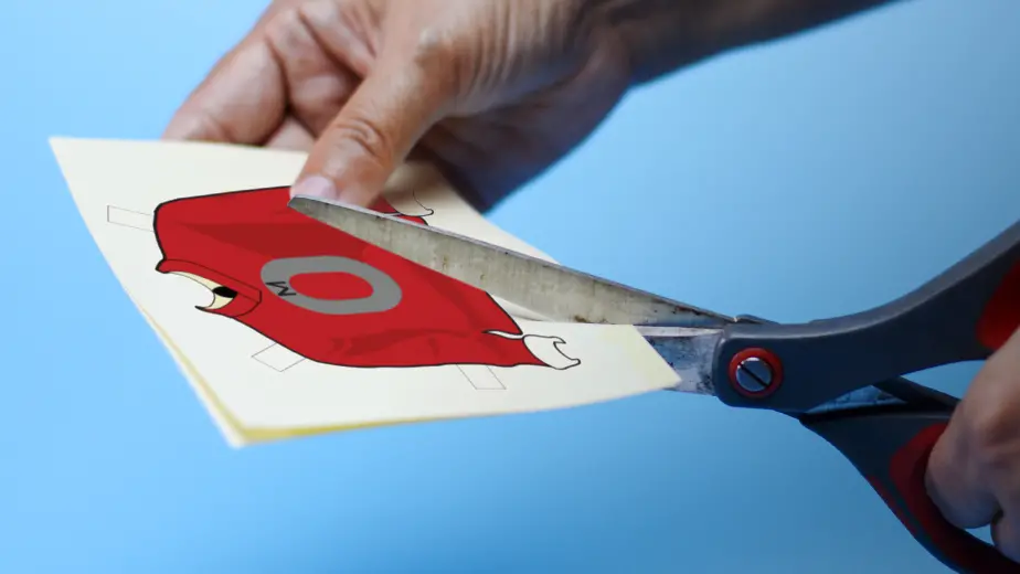Person using black scissors to cut out an OSU sweater for a paper doll