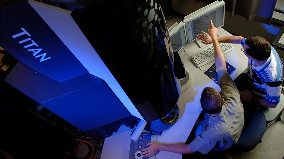 two researchers pointing at a computer screen in front of the Titan microscope