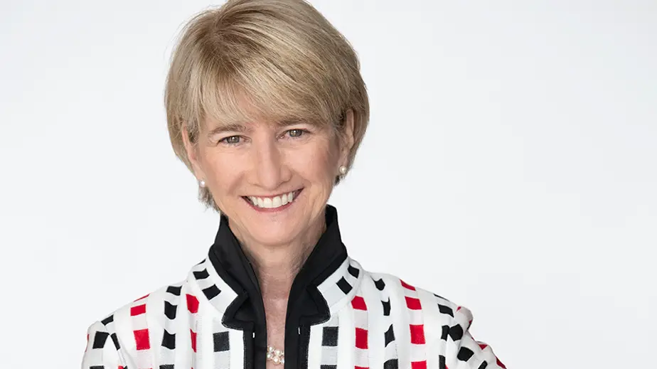 Ohio State President Kristina M. Johnson, a white woman with short blond hair, smiles warmly and wears a suit in this shot of her head and shoulders